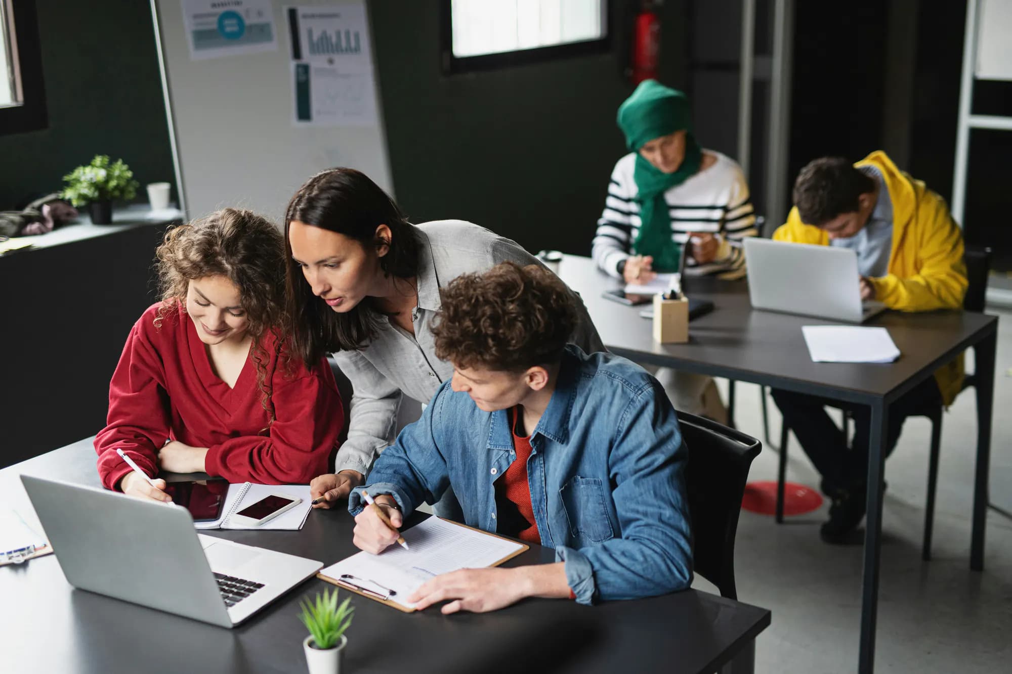 Une formatrice accompagne deux participants penchés sur leurs notes, en salle de formation